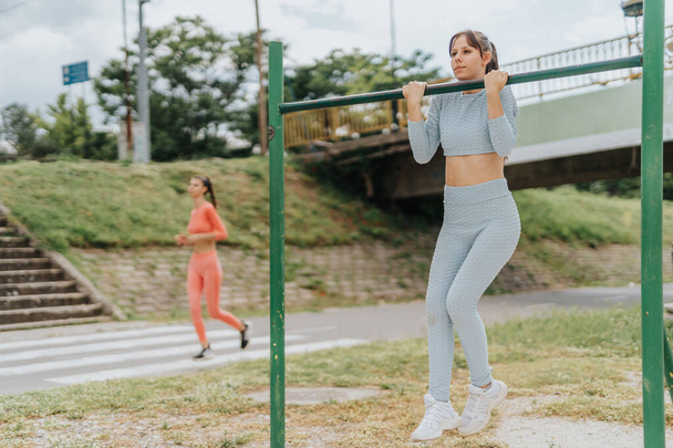 Fit girls exercise outdoors in a city park, inspiring each other with their energy and motivation. They perform cardio exercises, stretch their legs, and train their bodies in a sporty and urban city. - Photo, Image