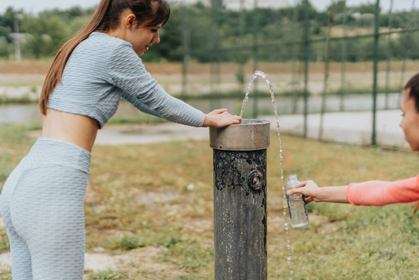 Κορίτσια πόσιμο νερό στο πάρκο από το σιντριβάνι μετά την εκπαίδευση. - Φωτογραφία, εικόνα