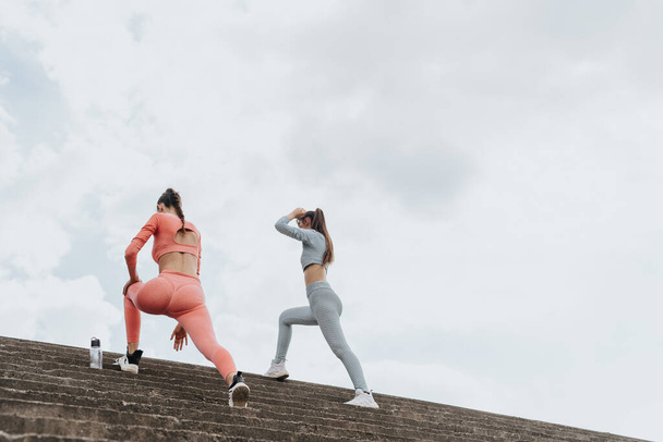 Un grupo de mujeres motivadas en ropa deportiva realizan un riguroso programa de entrenamiento al aire libre en las escaleras de un parque urbano. Inspiran un estilo de vida saludable y activo. - Foto, Imagen