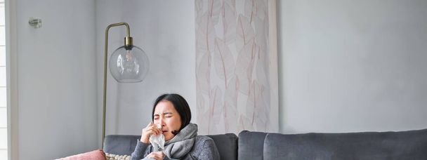 Korean woman feels unwell, sneezing and coughing, catching cold, staying at home with fever and temperature, taking medication. - Photo, Image