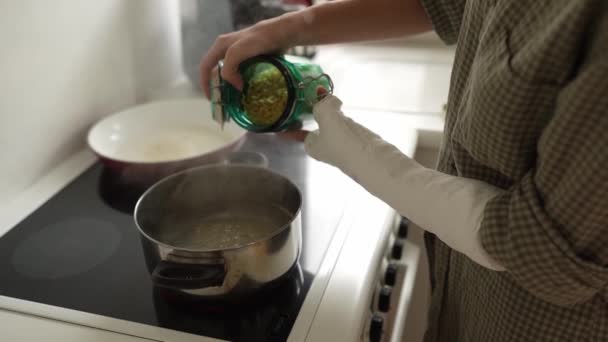 Nastolatka przygotowuje sobie lunch. Gotuje makaron na kuchence elektrycznej. dziewczęce dłonie, z tynkiem na jednym, wlać makaron ze szklanego słoika do wrzącej wody w rondlu. - Materiał filmowy, wideo