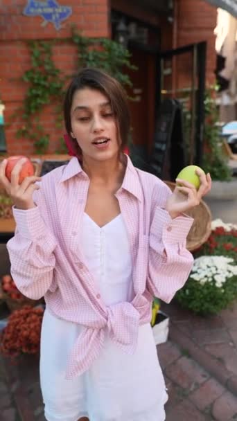 Eine elegante junge Dame, die als Verkäuferin auf dem Bauernmarkt arbeitet, beschreibt eloquent verschiedene Apfelsorten. Hochwertiges 4k Filmmaterial - Filmmaterial, Video