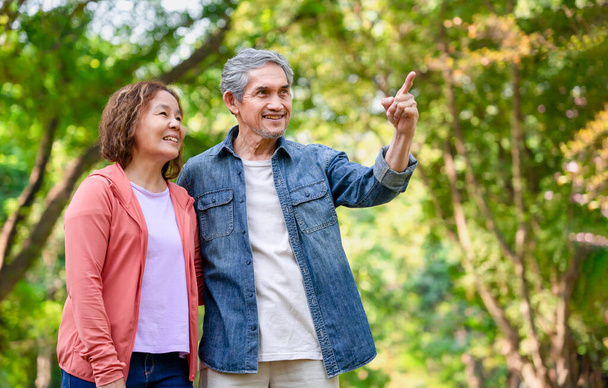 senior married couple spend leisure time in forest park,older adult male pointing index to something a mature female look up,and smiling together,concept of family,relationship,the love of a family - Foto, imagen