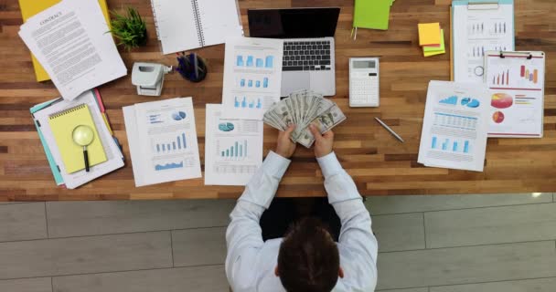 Podnikatel u stolu v obchodní kanceláři počítá peníze v ruce analyzuje grafy a grafy příjmů top view. Obchodní strategie a finanční příjmy a emoce bohatství - Záběry, video