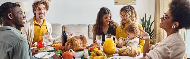 glückliche multirassische Familie und Freunde, die beim Thanksgiving-Dinner reden und lächeln, festliches Banner - Foto, Bild