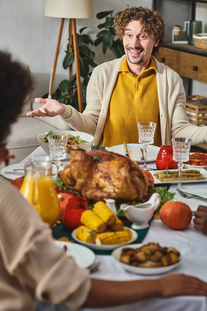 onnellinen mies elehtii ja puhuu kiitospäivän illallisen aikana perhepiirissä, paahdettu kalkkuna pöydällä - Valokuva, kuva