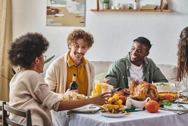 счастливая многонациональная семья и друзья разговаривают во время празднования Дня благодарения, праздничные мероприятия - Фото, изображение