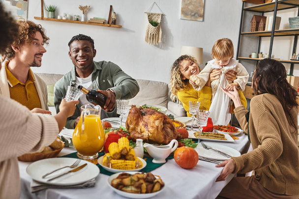african american man pouring wine into glass, multiethnic family celebrating Thanksgiving at home - Photo, Image