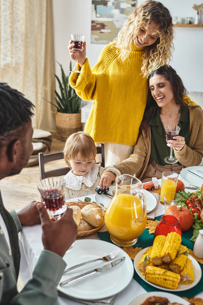 joyful lgbt couple celebrating Thanksgiving with toddler baby girl, cheering and laughing at home - Fotoğraf, Görsel