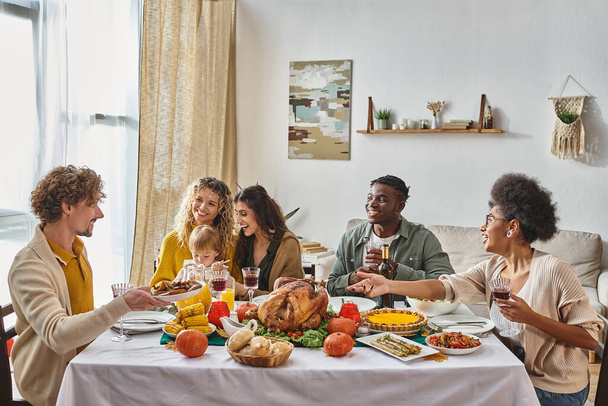 man passing plate with roasted potatoes to happy african american woman during Thanksgiving dinner - Foto, Bild