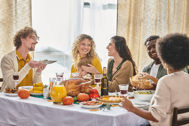 happy multiracial family and friends enjoying meals and drinks while gathering on Thanksgiving day - Photo, Image