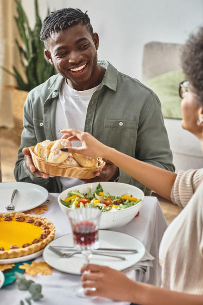 happy african american man looking at sister taking baked bun during Thanksgiving holiday - Photo, Image