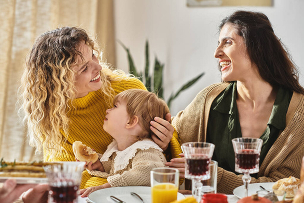 χαρούμενο λεσβιακό ζευγάρι και μικρό παιδί απολαμβάνουν νόστιμο δείπνο κατά τη διάρκεια των Ευχαριστιών - Φωτογραφία, εικόνα