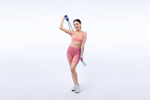 Młoda energiczna azjatycka kobieta w sportowej odzieży ze skaczącym lub pomijającym szlafrokiem pozująca do portretu w studiu nakręconym na odizolowanym tle. Narzędzie do ćwiczeń wytrzymałościowych i zdrowego trybu życia pielęgnacji ciała. Energiczny - Zdjęcie, obraz