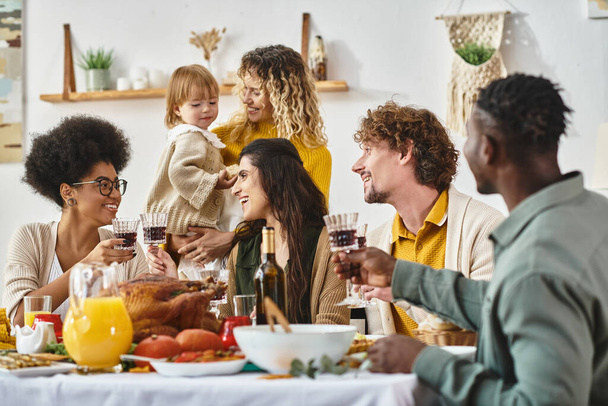 Gelukkige Thanksgiving, vrolijke multi-etnische vrouwen klinkende glazen wijn in de buurt van vrienden en familie - Foto, afbeelding
