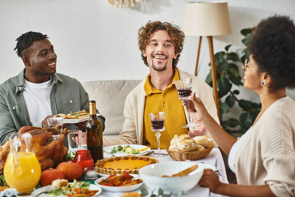 Feliz Día de Acción de Gracias, alegres amigos multiétnicos charlando en la mesa de banquetes con pavo asado - Foto, Imagen