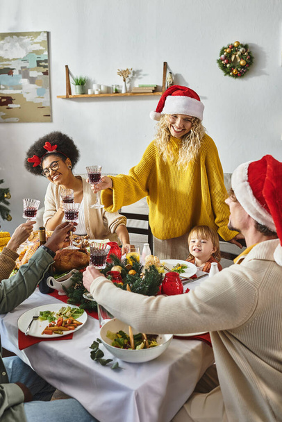 Onnellinen monikansallinen ystävät ja perhe joulupukki hatut clinking lasit ja juhlii Hyvää joulua - Valokuva, kuva