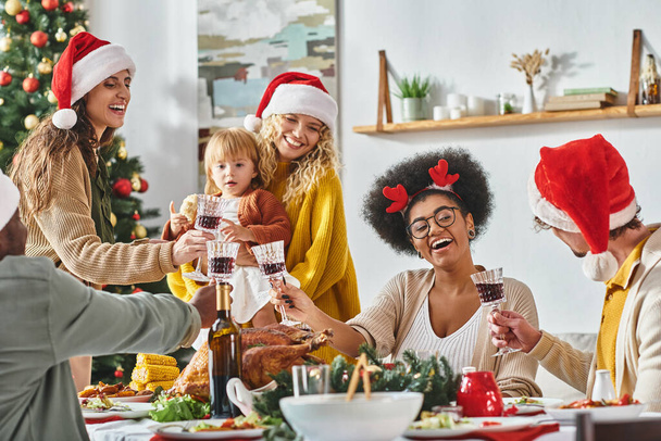 grande famille multiethnique joyeuse accrochant leurs lunettes à la table de fête portant des chapeaux de Père Noël, Noël - Photo, image