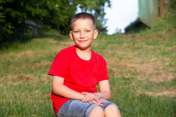 Egy piros pólós fiú ül a nyári természet hátterében.. - Fotó, kép
