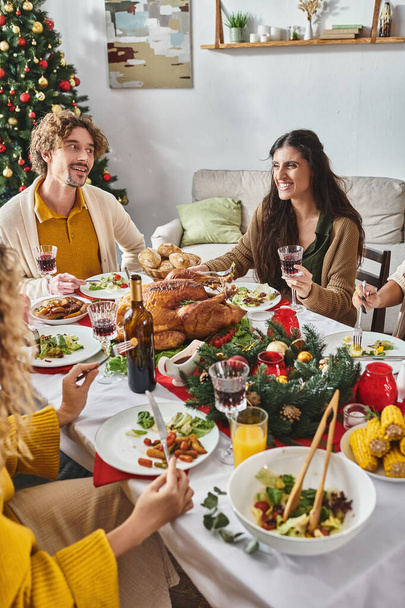 recortado ver multirracial familia disfrutando de vacaciones almuerzo y sonriendo con árbol de Navidad en el telón de fondo - Foto, imagen