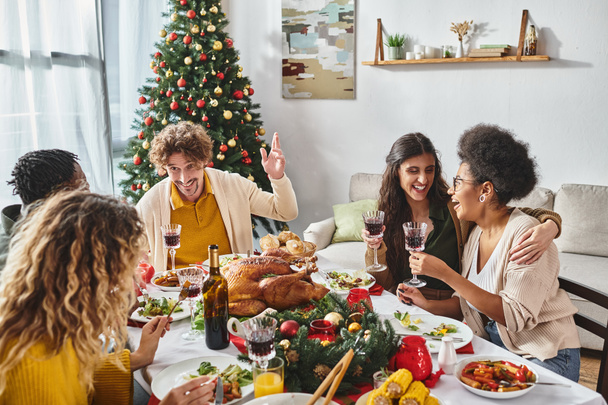 felices parientes multiculturales celebrando la Navidad juntos y disfrutando de un almuerzo festivo y vino - Foto, Imagen