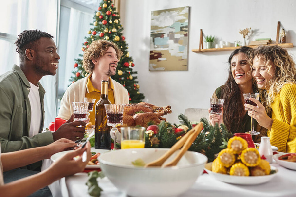 クリスマスツリーバックドロップとトルコとワインで休日の饗宴を楽しむ喜びの多民族家族 - 写真・画像