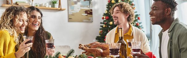 feliz familia multirracial riendo y disfrutando del almuerzo con pavo y vino, Navidad, pancarta - Foto, Imagen