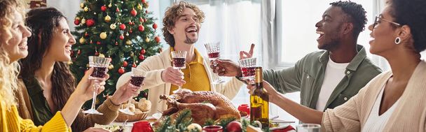 πολυπολιτισμική οικογένεια gesturing και γέλιο κάθεται στο εορταστικό τραπέζι γιορτάζει τα Χριστούγεννα, πανό - Φωτογραφία, εικόνα