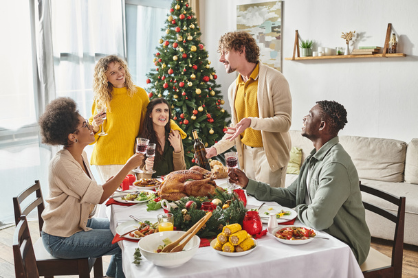 joyous family members sitting at Christmas table with turkey and wine laughing and talking actively - Photo, Image
