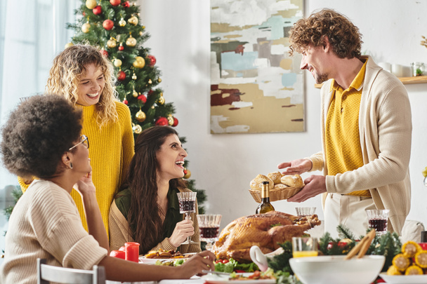 jeune homme joyeux tenant assiette de pain entouré par sa famille multiethnique, toile de fond de sapin de Noël - Photo, image