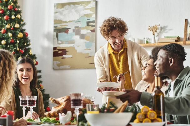 Büyük, neşeli, çok kültürlü bir aile Noel masasında oturmuş gülüyor ve bayram şöleninin tadını çıkarıyor. - Fotoğraf, Görsel