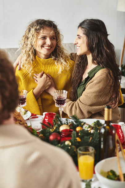 sweet lgbt couple holding hands and looking cheerfully at each other sitting at Christmas table - Photo, Image