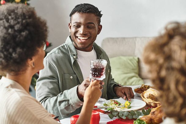 alegre hombre afroamericano sentado a la mesa festiva rodeado de sus parientes, Navidad - Foto, Imagen