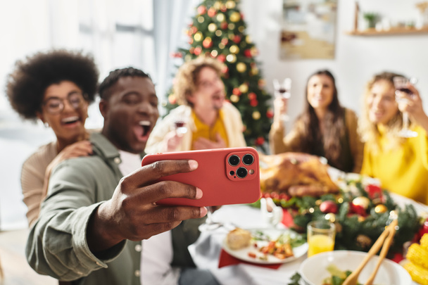 gelukkig multi-etnische familieleden nemen selfie aan feestelijke tafel met wijn en voedsel, wazig decor - Foto, afbeelding