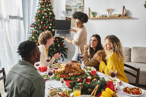 ホリデーテーブル,クリスマスでラップトップカメラで積極的かつ笑顔で話す多民族家族 - 写真・画像