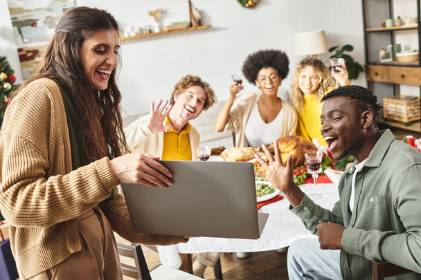 multiraciální veselí příbuzní sedící na vánoční hostině jásající a usmívající se na notebook kamery - Fotografie, Obrázek
