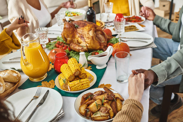 vue dégagée famille multiethnique priant ensemble à table festive avec dinde et vin, Thanksgiving - Photo, image