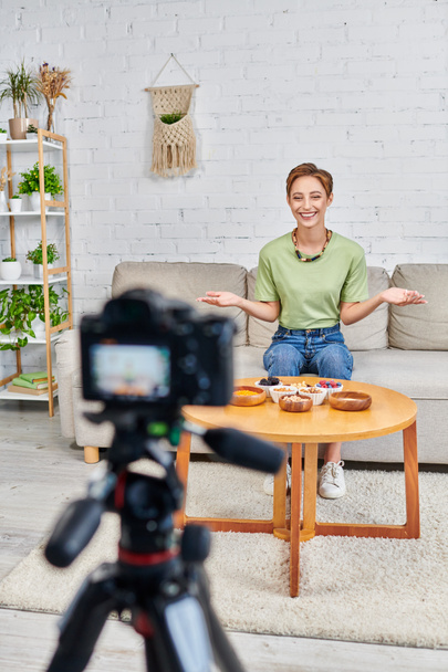 mujer feliz presentando productos vegetarianos cerca de la cámara digital borrosa, las dietas a base de plantas video blog - Foto, Imagen