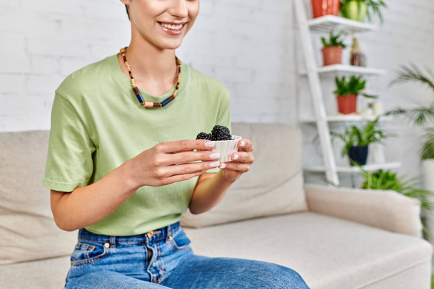 vista cortada de mulher vegetariana sorridente com tigela de amoras maduras, conceito de dietas à base de plantas - Foto, Imagem
