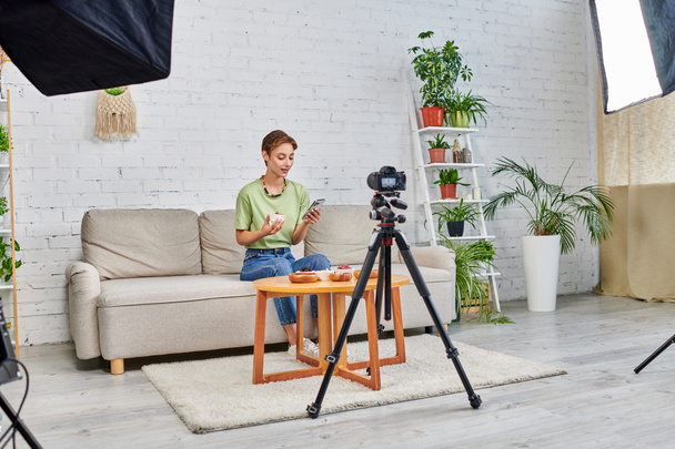 video blogger con smartphone cerca de comida vegetariana y cámara digital con lámpara softbox en casa - Foto, Imagen