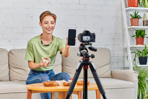 felice donna vegetariana in possesso di smartphone con schermo bianco durante il video blog su diete a base vegetale - Foto, immagini
