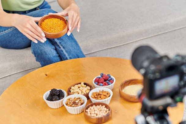 cropped woman with bowl of lentils near table with fresh berries and nuts in front of digital camera - Photo, Image