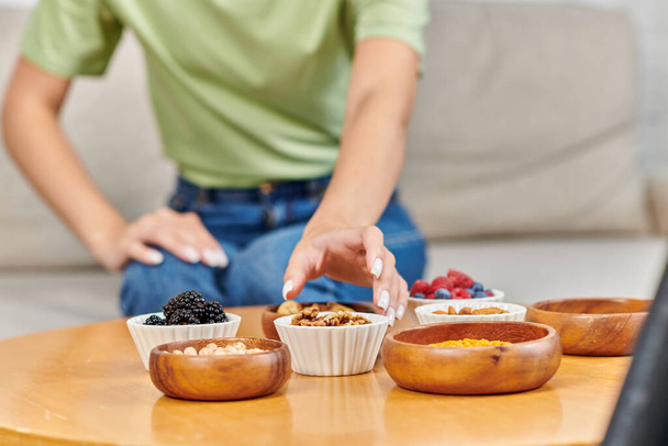 обрезанная размытая женщина берет чашу грецких орехов рядом со свежими ягодами и бобовыми на столе, вегетарианство - Фото, изображение