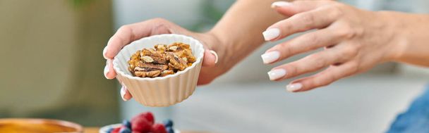 cropped view of vegetarian woman holding bowl with walnuts, plant-based diets concept, banner - 写真・画像