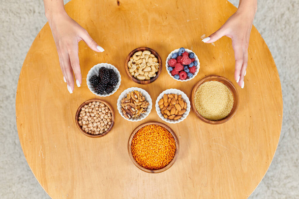 vista superior de las manos femeninas sobre la mesa con una variedad de alimentos vegetarianos a base de plantas en la mesa en casa - Foto, Imagen