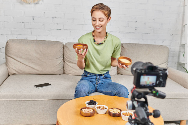 donna felice con ciotole di couscous e lenticchie vicino alla fotocamera digitale e vari alimenti a base vegetale - Foto, immagini