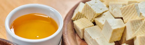 close of tofu cheese on wooden plate and ceramic bowl with olive oil, vegetarian concept, banner - Photo, Image