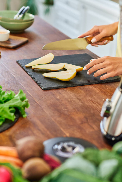 partial view of vegetarian woman with knife near ripe sliced pear on chopping board in kitchen - Photo, Image