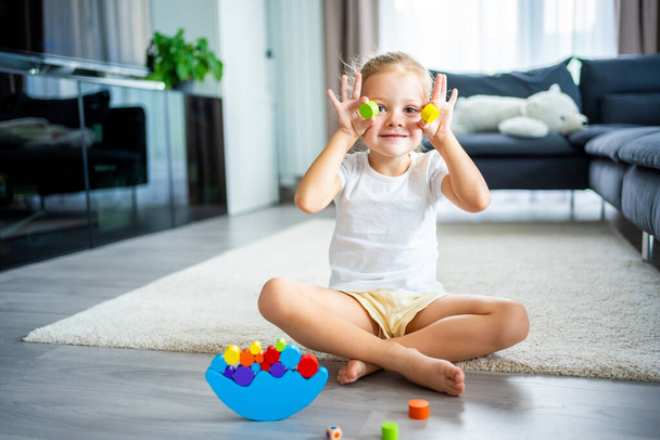 Niña jugando con el juguete de equilibrio de madera en el suelo en la sala de estar en casa. Foto de alta calidad - Foto, imagen