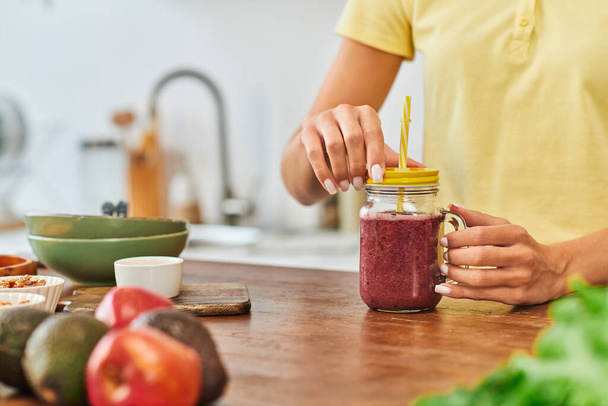 cropped view of woman near mason jar with delicious plant-based smoothie near blurred fresh fruits - Photo, Image
